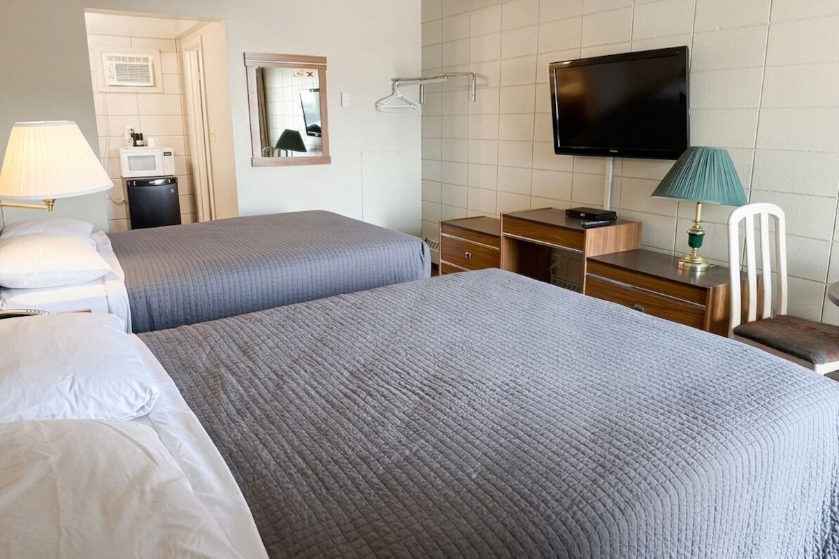 Una habitación de hotel con dos camas, televisión, escritorio y una silla.