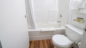 Un baño con bañera, inodoro y un estante con artículos de aseo.