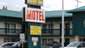 Een motel met een bord waarop staat Good Knight Inn, een bord voor een keuken en een parkeerplaats met meerdere voertuigen.