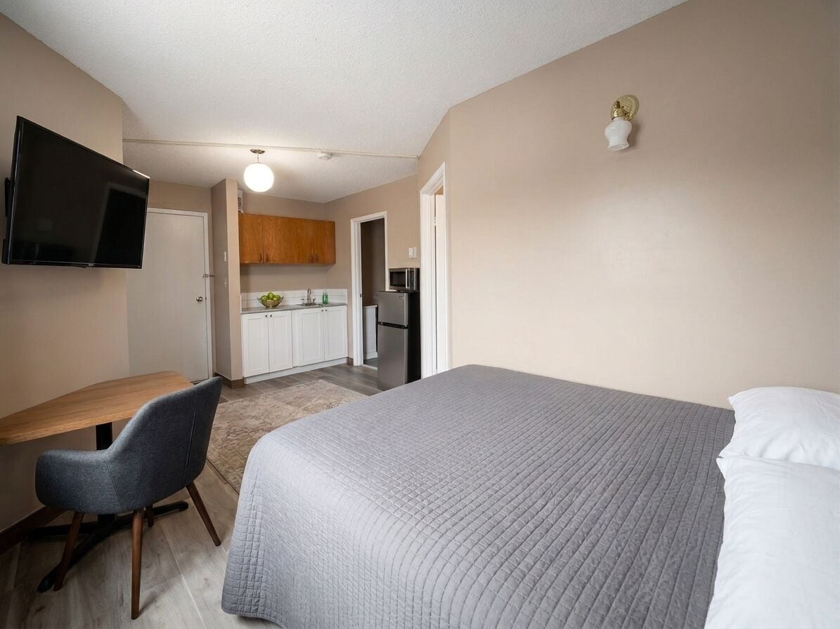 A compact bedroom with a bed, a desk, and a chair. A television is mounted on the wall.