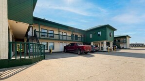 Un motel con fachada verde, un estacionamiento y una camioneta roja estacionada al frente.