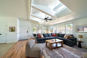 A spacious living room with a ceiling fan, a sectional sofa, a coffee table, and a patterned rug.