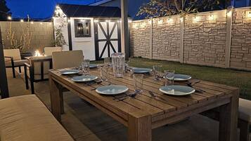 Een buiten eethoek met een houten tafel gedekt voor zes personen, omringd door stoelen en een stenen muur.