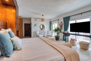 A bedroom with a large bed, a television, a potted plant, and a view of the outdoors. - Luxury two-story penthouse condo at the beach in the heart of Punta de Mita! (Punta de Mita)