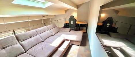 Un intérieur moderne avec un canapé d’angle, un bureau et des fauteuils de jeu.