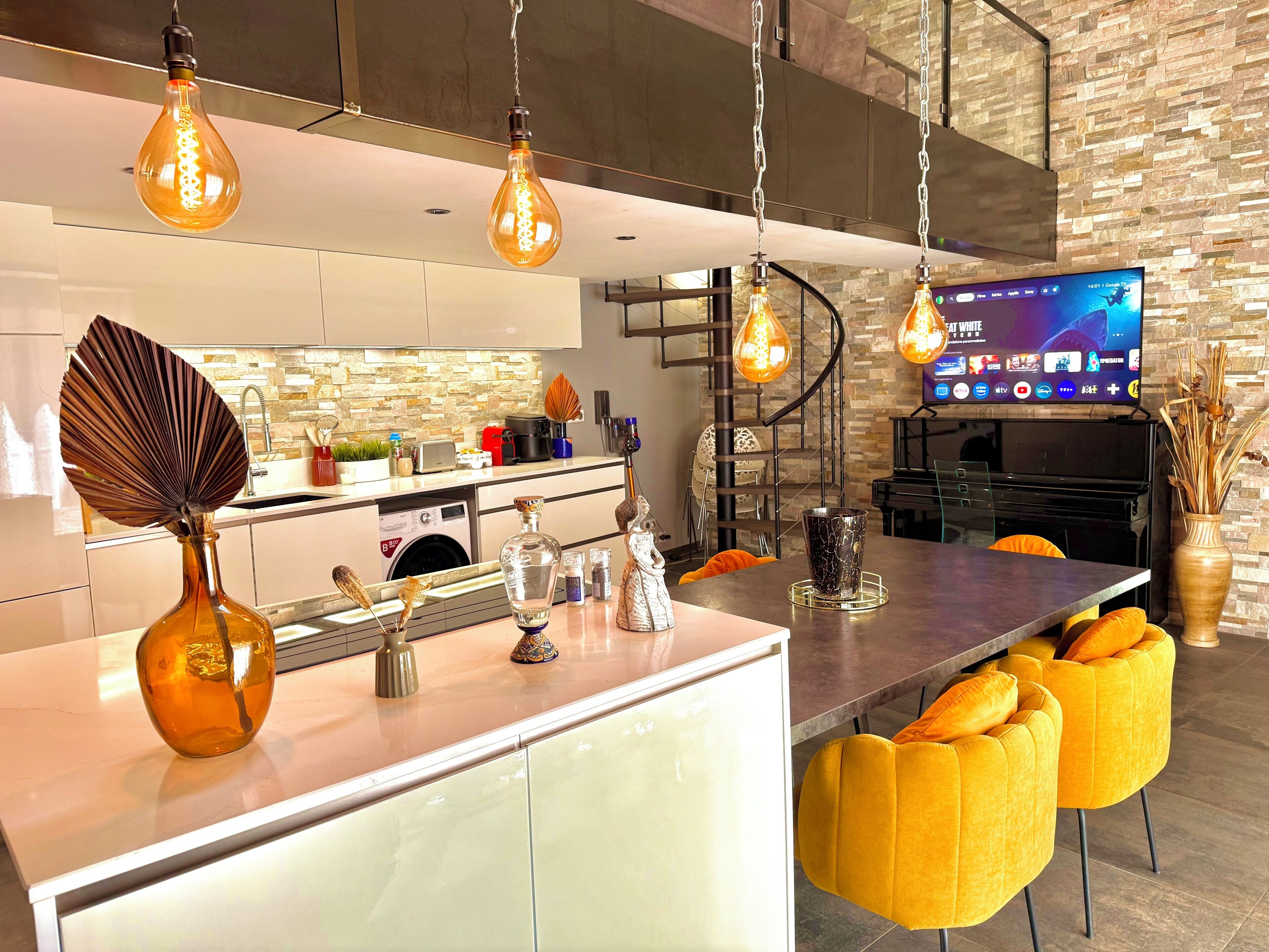 A modern kitchen with a central island, a built-in washing machine, and a flat-screen TV mounted on the wall.