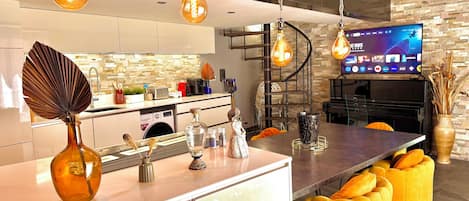 A modern kitchen with a central island, a built-in washing machine, and a flat-screen TV mounted on the wall.