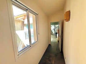 Ein schmaler Flur mit einem großen Fenster links, einer Tür rechts und einer Treppe im Hintergrund.