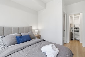 Ein modernes Schlafzimmer mit einem großen Bett, einem Nachttisch mit Lampe und einem begehbaren Kleiderschrank.