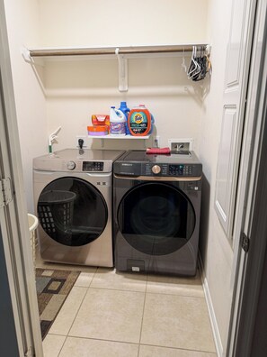 Una sala de bugaderia amb dues rentadores de càrrega frontal, una estant amb ampolles de detergent i un escuraprius.