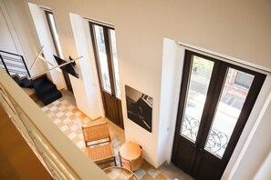 A high-ceilinged room with a checkered floor, a wicker chair, a small round table, and a door with a metal gate. - San Felipe 668 (Guadalajara)