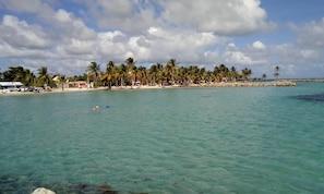 A beach with clear turquoise water, palm trees, and a rocky outcrop. - BEAUVALETTE SOLEIL (Sainte-Anne)