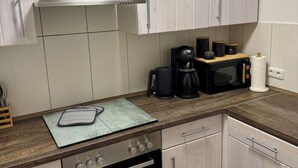 Une cuisine moderne avec des meubles en bois clair, une hotte de cuisinière en acier inoxydable, un four encastré, un four à micro-ondes et une machine à café.