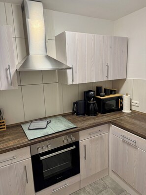 Eine moderne Küche mit hellen Holzschränken, einer Edelstahl-Dunstabzugshaube, einem Einbauofen, einer Mikrowelle und einer Kaffeemaschine.