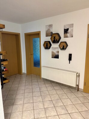 A hallway with a tiled floor, wooden doors, a radiator, and wall-mounted artwork. - Westerhäuser Vacation Rentals – Apartment Schmuckstück – Family Apartment in the Harz Mountains (Thale)