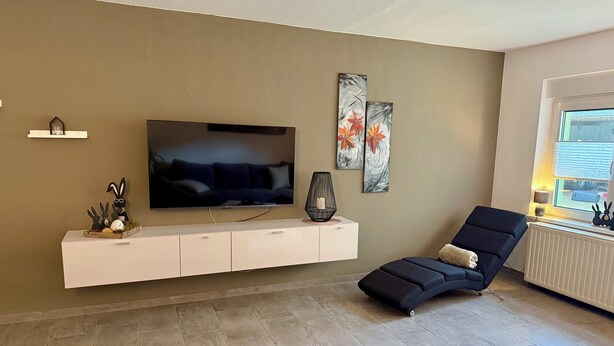 Un salon doté d’un téléviseur à écran plat, d’un fauteuil inclinable, d’un meuble de rangement blanc et d’œuvres d’art accrochées au mur.