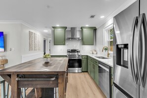 A modern kitchen with green cabinets, stainless steel appliances, and a wooden island. - The Lightkeeper's Cottage Beaufort, SC (Beaufort)