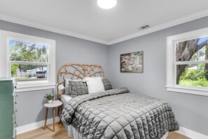 A bedroom with a bed, a bedside table with a lamp, and a window with a view of trees. - The Lightkeeper's Cottage Beaufort, SC (Beaufort)
