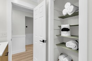 Een hotelkamer met een witte deur, een houten vloer en planken met netjes opgevouwen handdoeken.