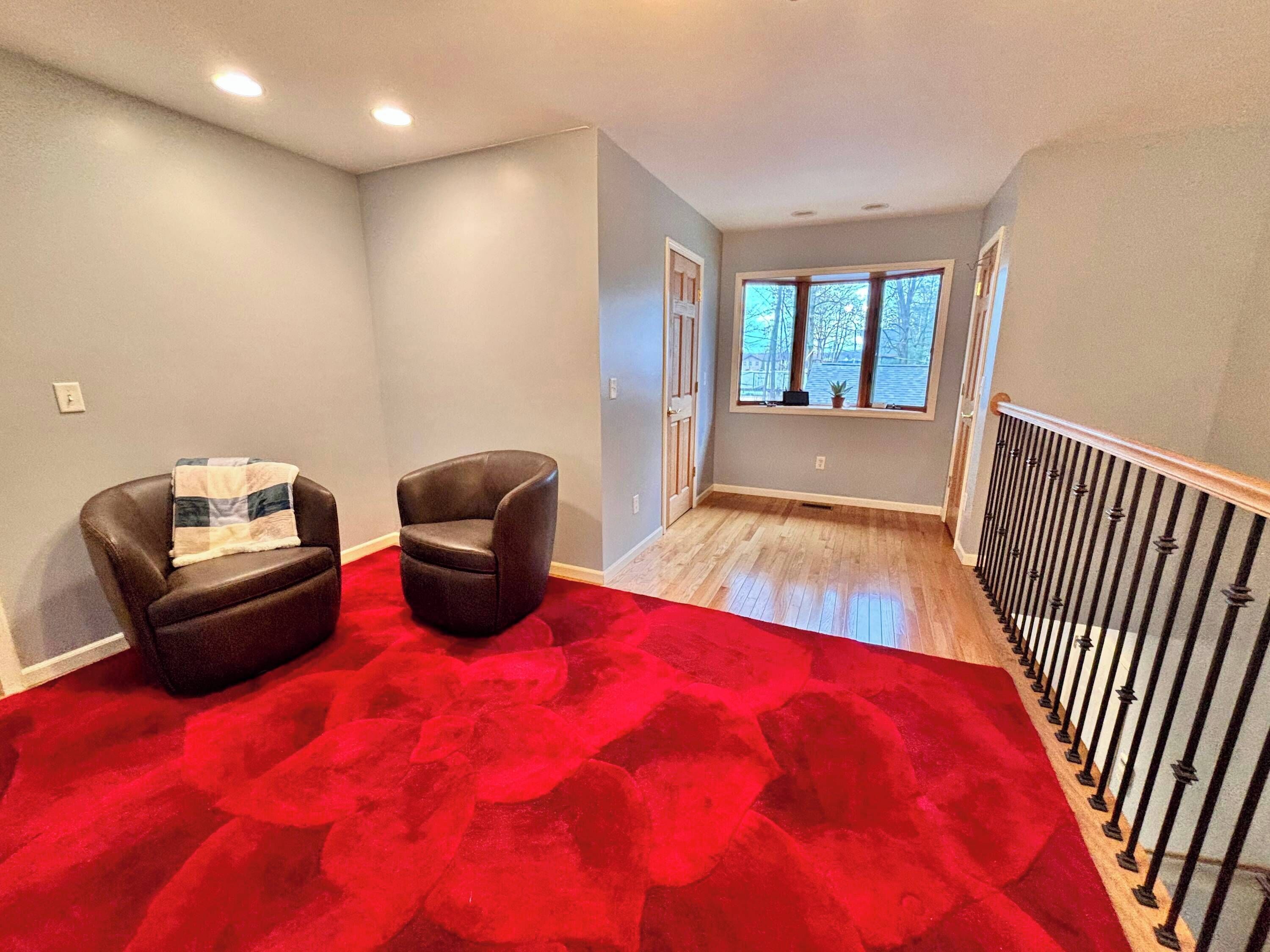 Een kamer met een rood tapijt, twee leren fauteuils, een raam met uitzicht en een houten balustrade.