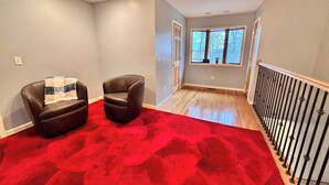 A room with a red carpet, two leather chairs, a window with a view, and a wooden railing. - Spacious Retreat w Lake access, Jacuzzi tub (Prudenville)