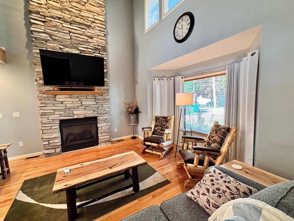 A living room with a stone fireplace, a flat-screen TV, a sofa, and a window with curtains.