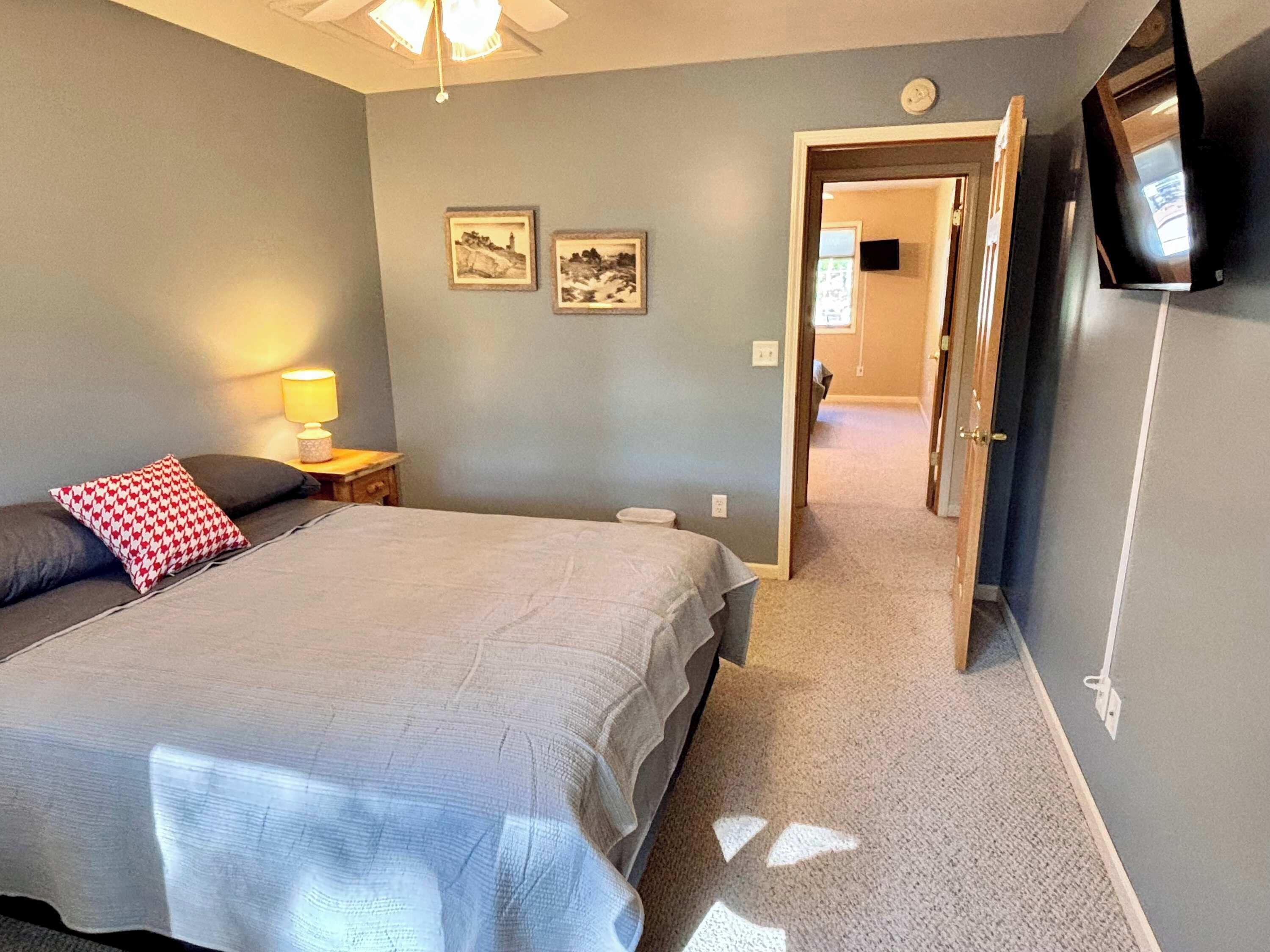 A bedroom with a bed, bedside table, lamp, and a television on the wall.