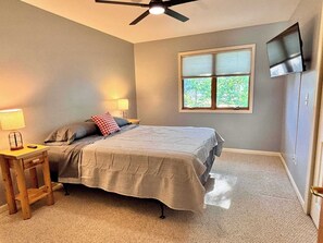 A bedroom with a bed, bedside lamps, a nightstand, a window, and a ceiling fan.