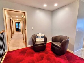 Un couloir avec une moquette rouge, deux fauteuils en cuir et une porte donnant sur une autre pièce.