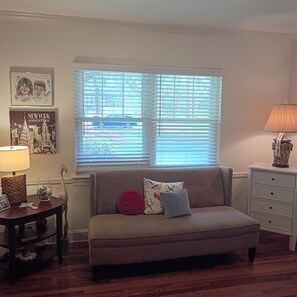 A living room with a sofa, a lamp, a side table, and a window with blinds. - Relax on Isle of Hope 30 Day Executive Rental (Savannah)