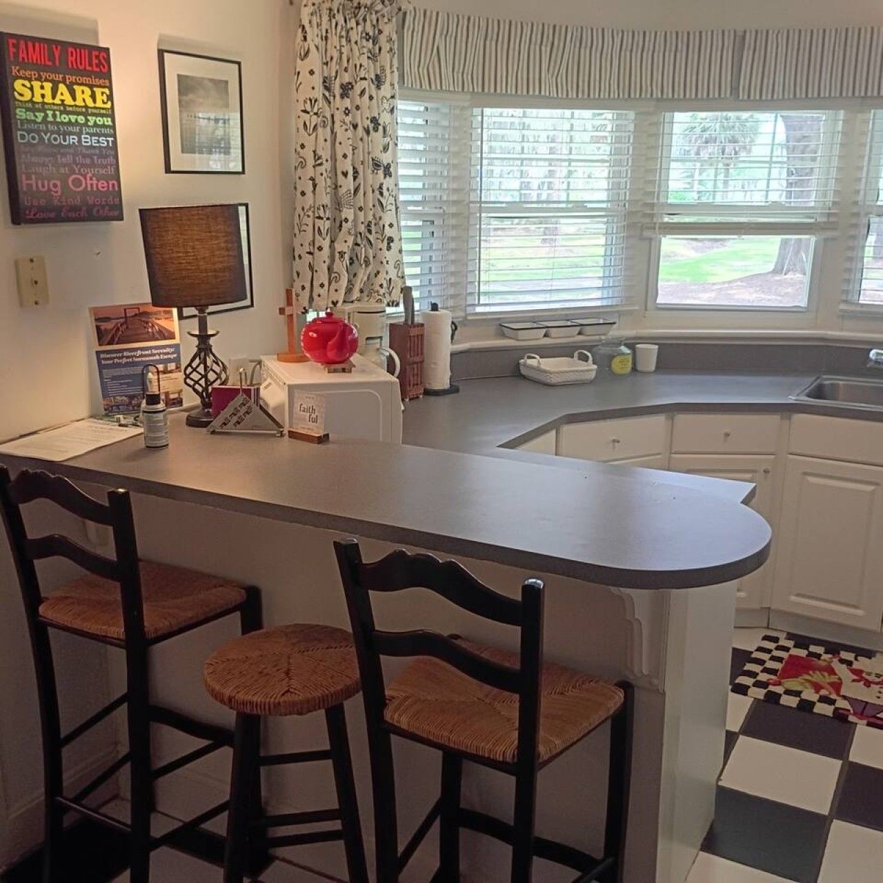 A kitchen with a curved island, two bar stools, a window with blinds, and a checkered floor.