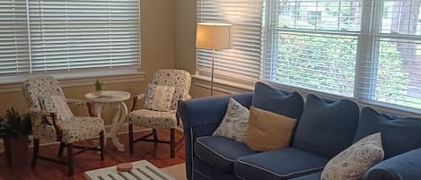 Una sala de estar con un sofá azul, sillones estampados, una mesita redonda y una lámpara de pie.