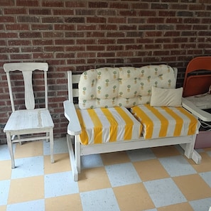 Ein Zimmer mit Schachbrettmuster-Boden, einem weißen Sofa mit gelb-weißen Kissen und einem weißen Sessel.