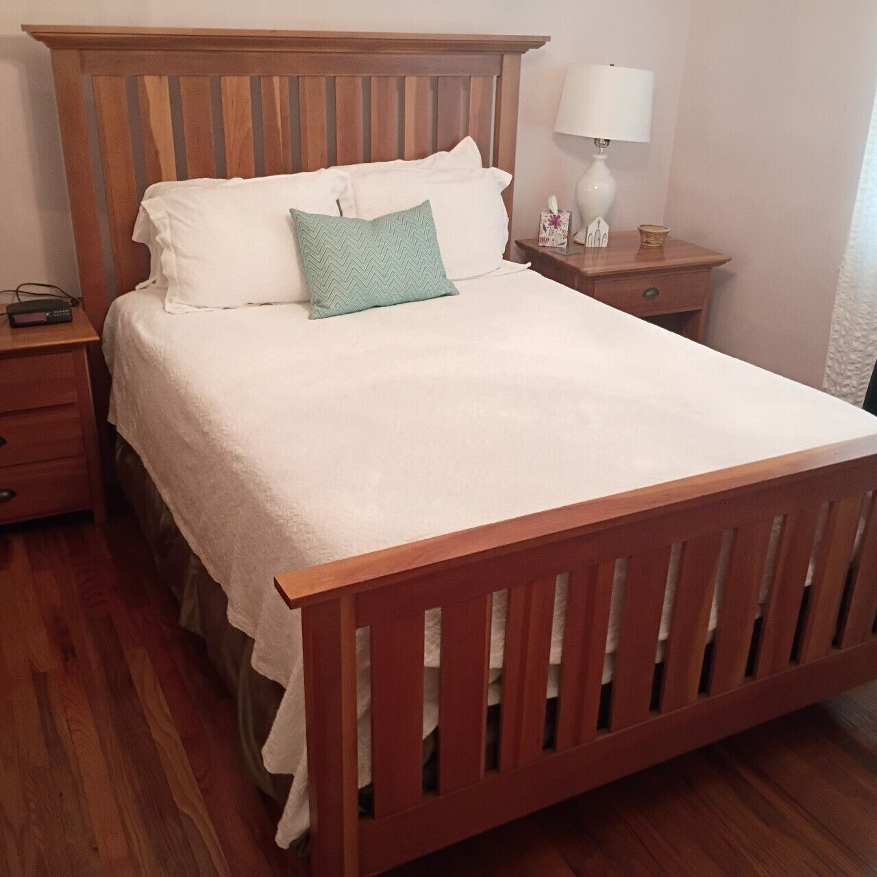 A single bed with a wooden headboard, a bedside table with a lamp, and a nightstand with a radio.