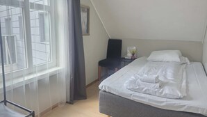 A bedroom with a bed, a chair, a small table, and a window with curtains.