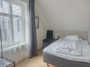 A bedroom with a bed, a chair, a small table, and a window with curtains.