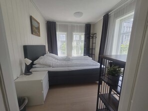 Ein Schlafzimmer mit Bett, Nachttisch, Lampe und einem Fenster mit Vorhängen.