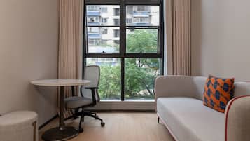 A room with a sofa, a small round table, a chair, and a window with a view of buildings and trees.