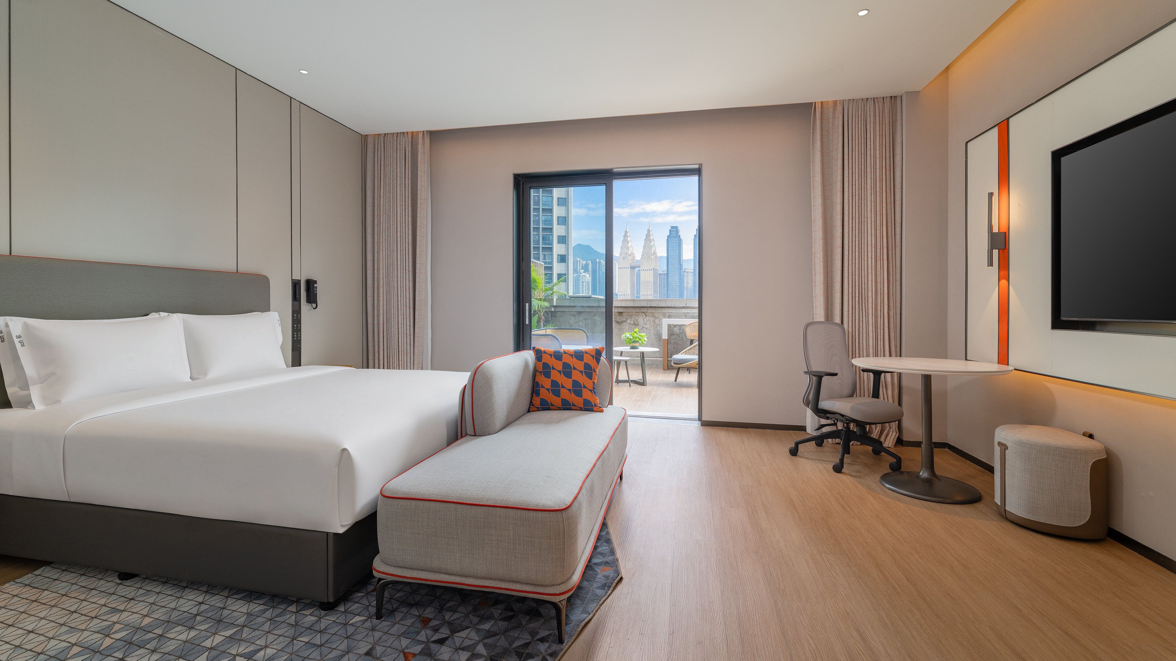A hotel room with a large bed, a desk with a chair, a small table, and a television.
