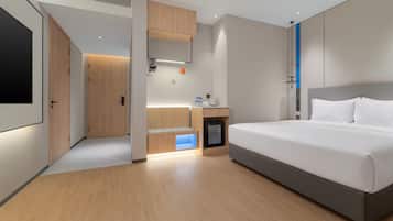 A modern hotel room with a large bed, a built-in desk, and a minibar.