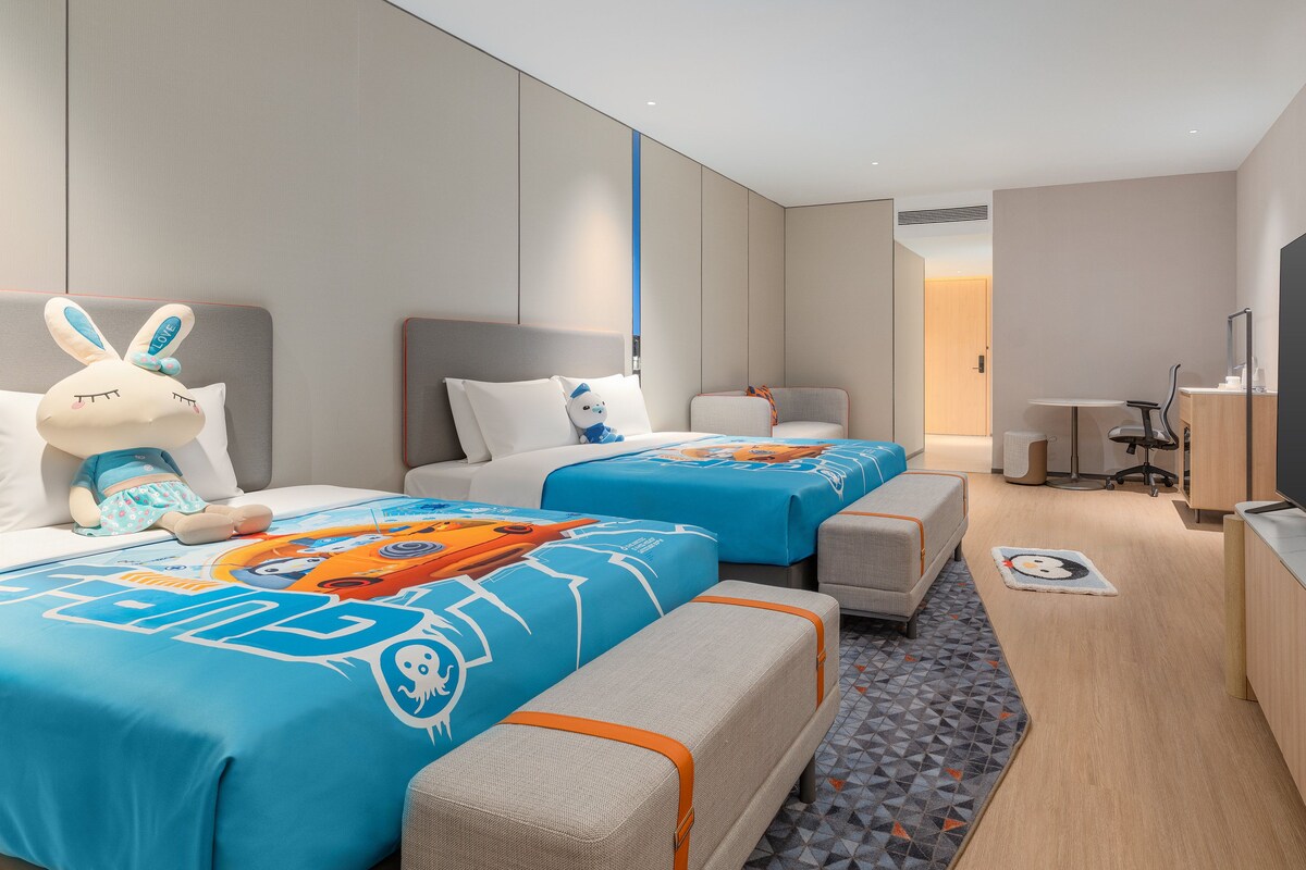 Ein Hotelzimmer mit zwei Betten, einem Fernseher, einem Schreibtisch und einem großen Fenster.