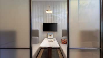 Quarto de hotel moderno com televisão de tela plana na parede, uma pequena mesa com um CD emoldurado e dois sofás com almofadas.