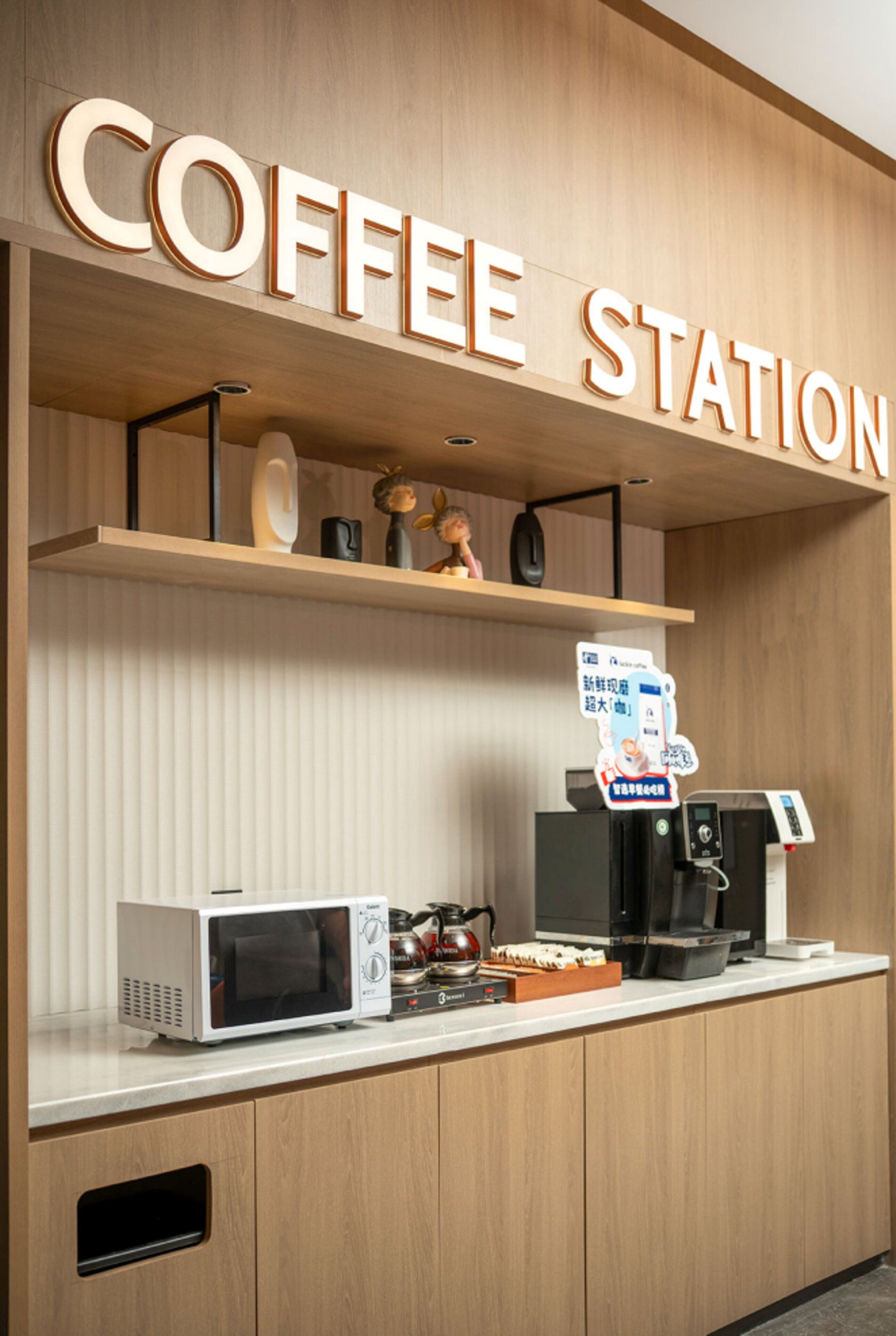 A coffee station with a sign reading 'COFFEE STATION,' a microwave, a coffee machine, and a kettle on the counter.