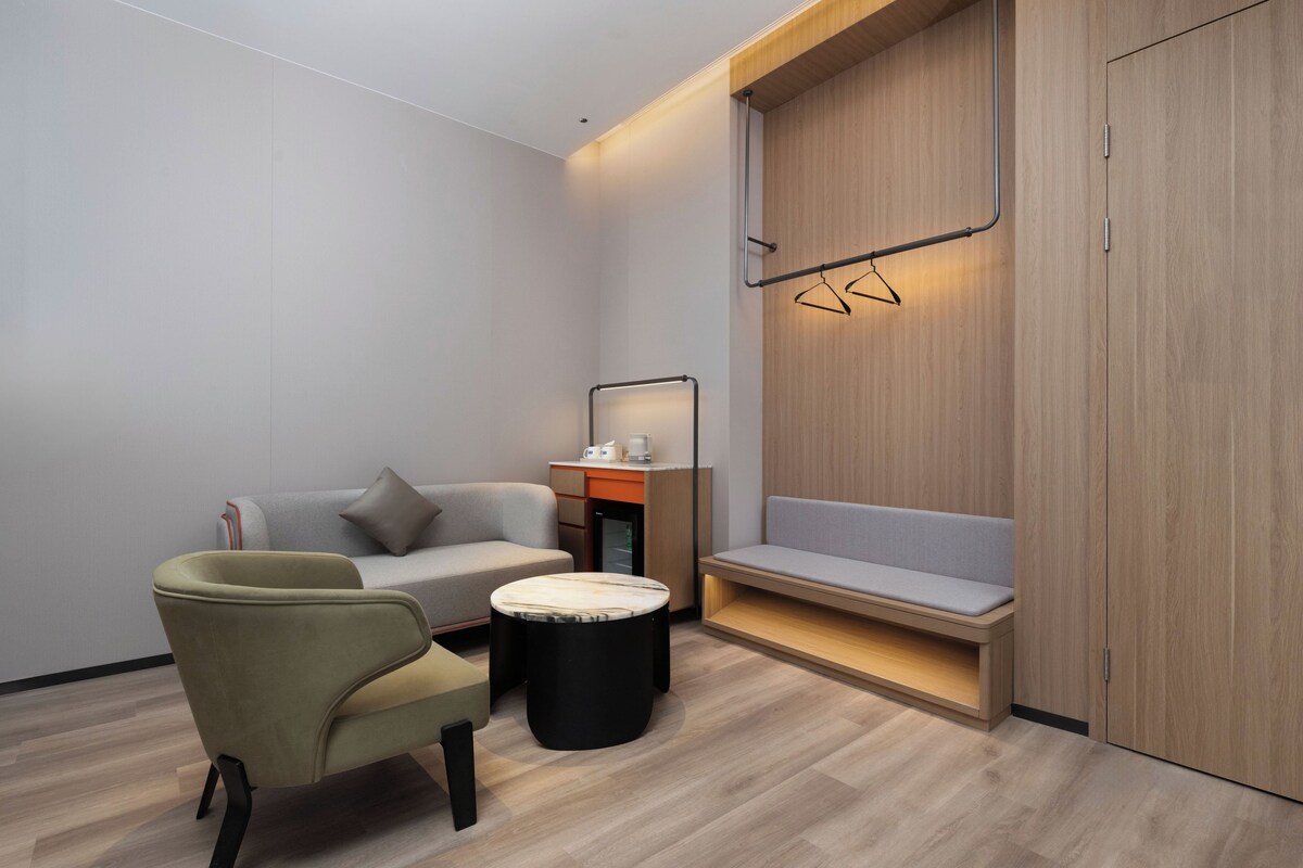 A modern room with a sofa, armchair, small round table, and a bench with a wooden wall and hanging clothes rack.