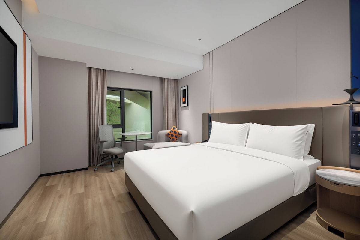 Habitació d'hotel moderna amb un llit gran, una taula de treball, una cadira i una finestra amb cortines.