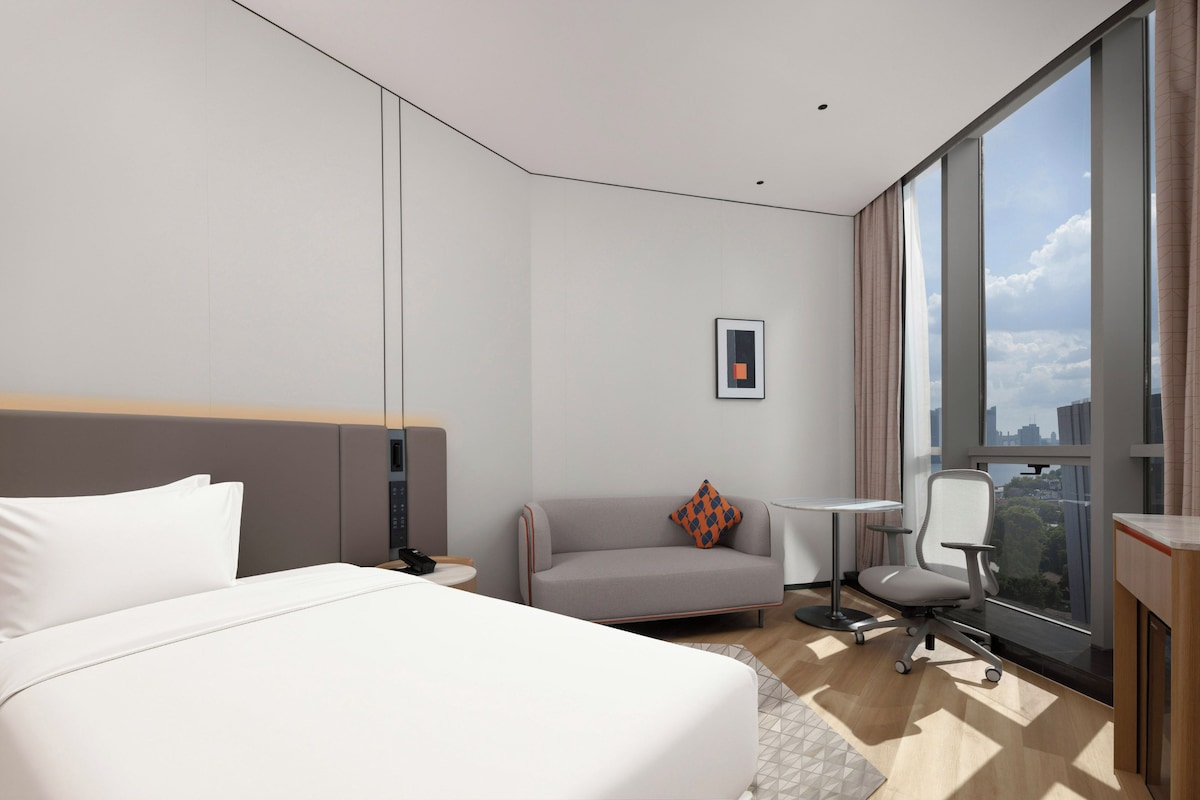 Una habitación de hotel moderna con una cama grande, un sofá pequeño, un escritorio y una silla.