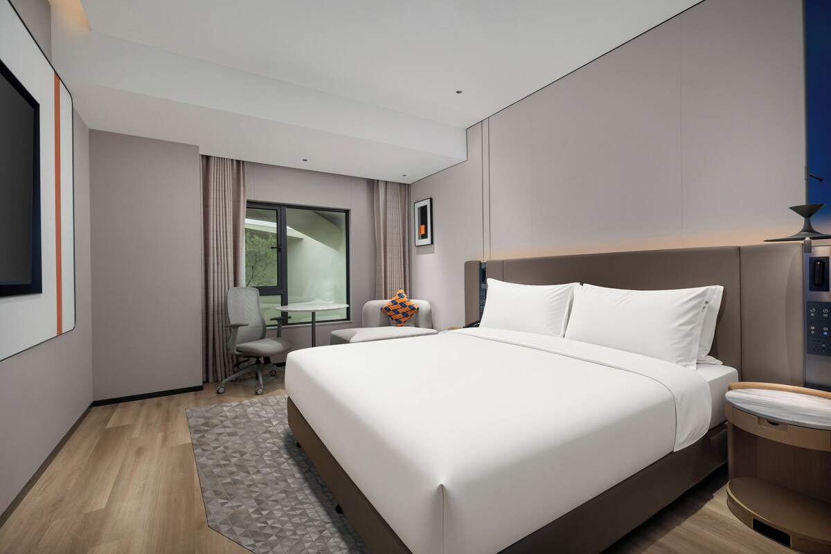 A modern hotel room with a large bed, a desk, and a chair.