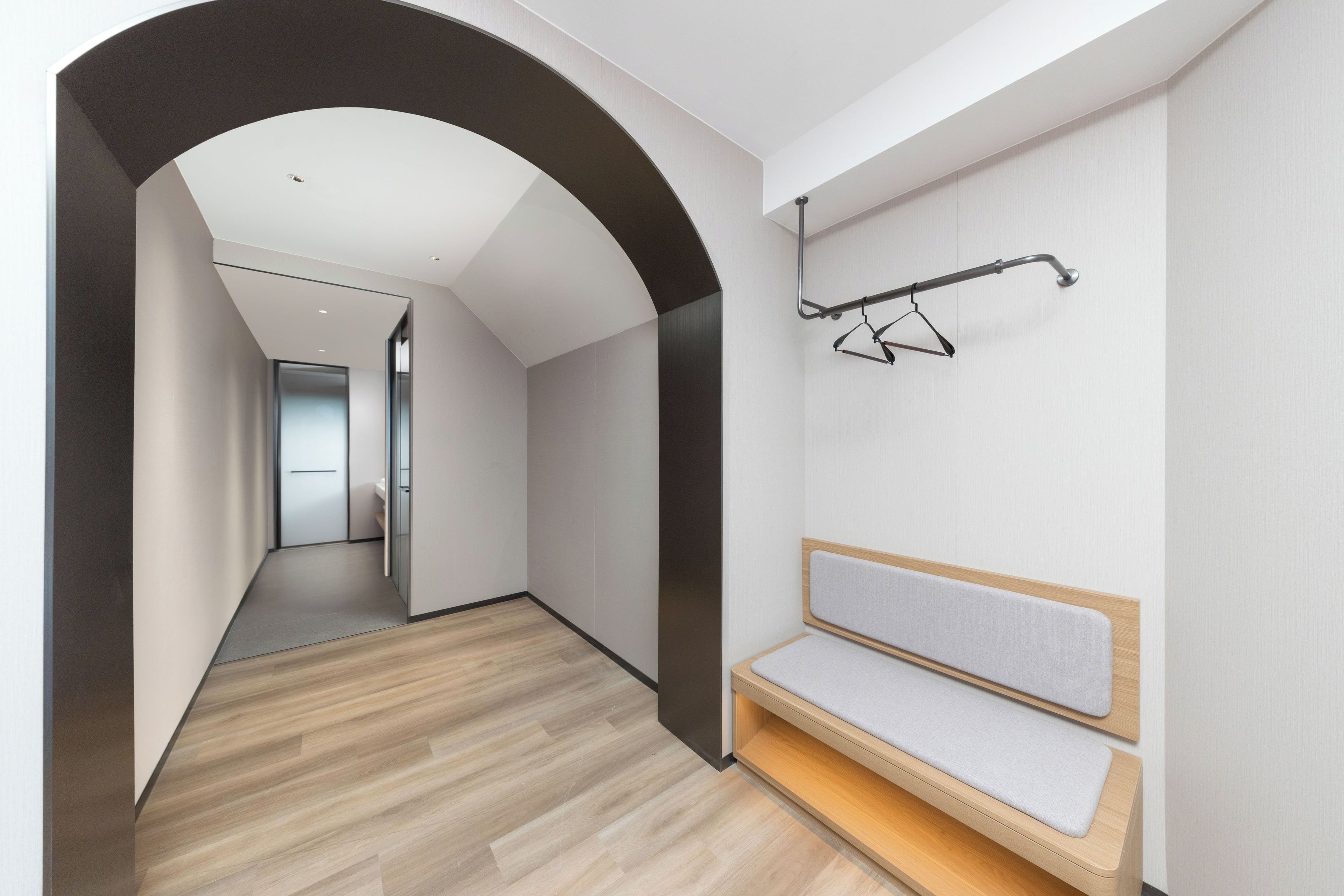Um corredor com um banco, um cabide e uma porta que dá para outro quarto.