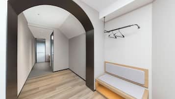 Um corredor com um banco, um cabide e uma porta que dá para outro quarto.
