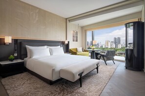 Una habitación de hotel moderna con una cama grande, una mesita, un sillón amarillo y un balcón con vistas a la ciudad.